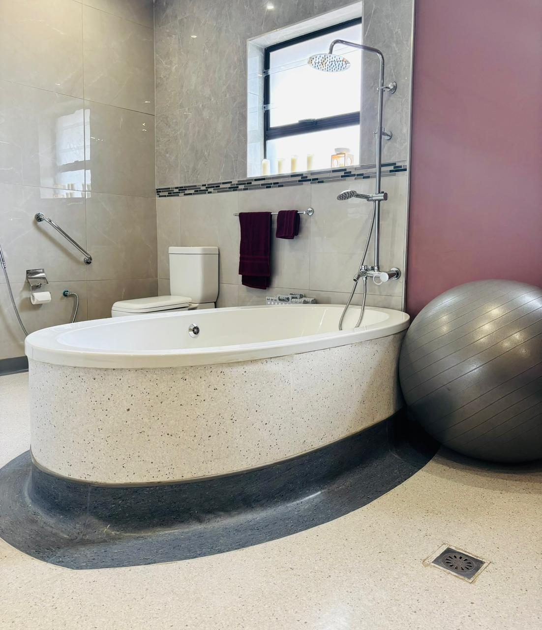 The birthing bath at Essence: a deep freestanding tub with a rain shower, grab rail and a birth ball beside it