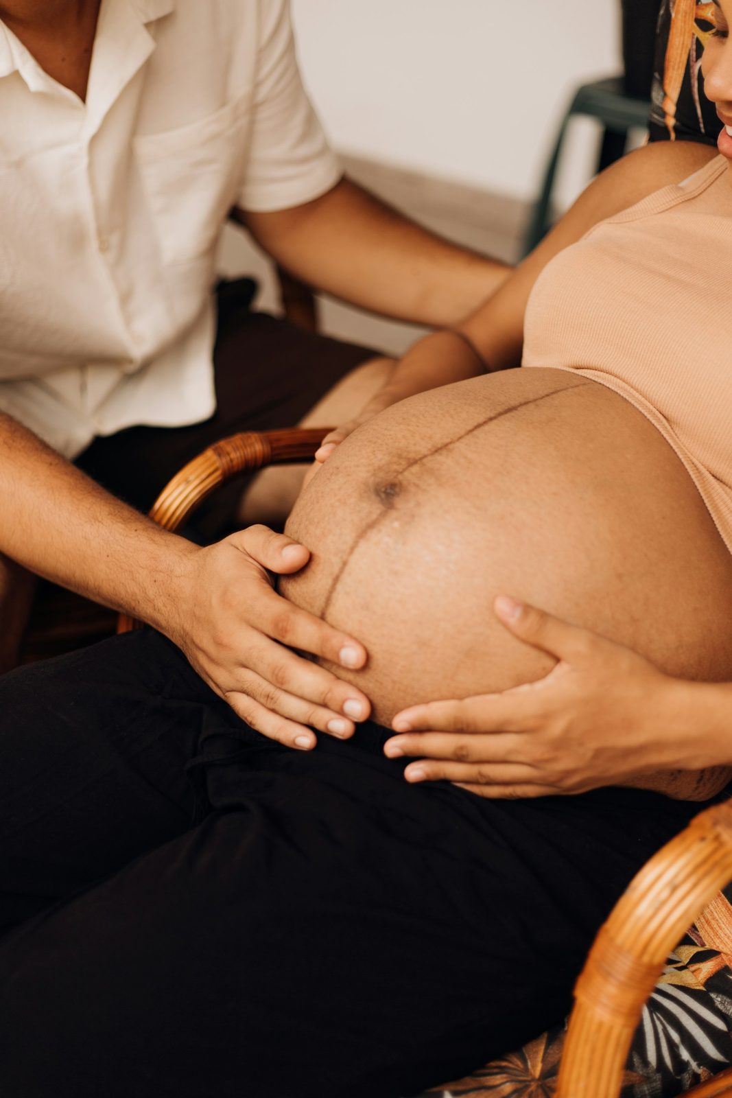 A pregnant woman seated, with a partner’s hands on her belly